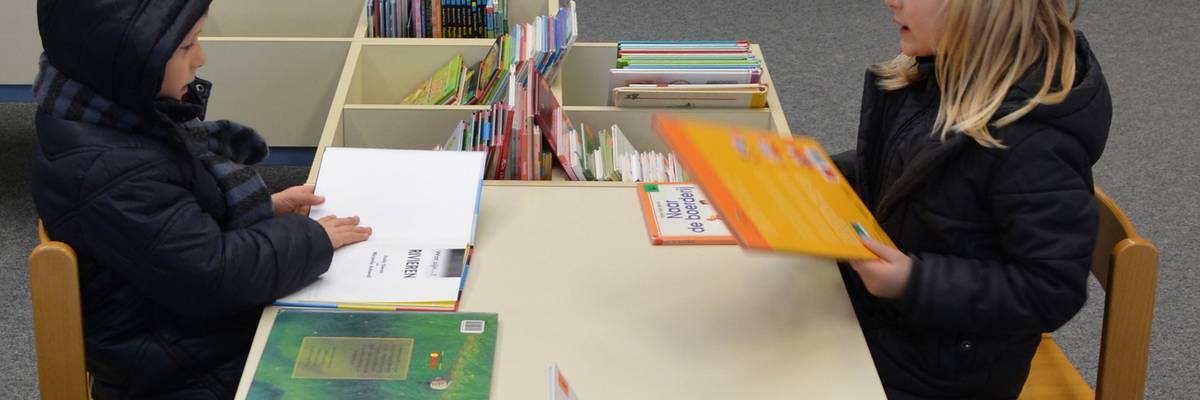 Zwei Kinder sitzen sich gegenüber und schauen sich Bücher an