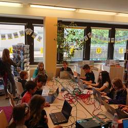 Kinder sitzen um einen Tisch und bauen an Laptops Welten in Minecraft