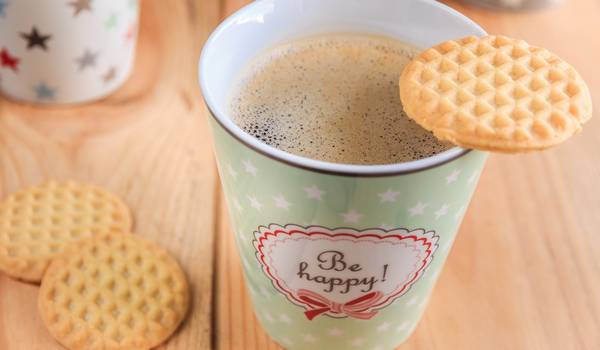 Kaffeebecher mit dem Aufdruck "be happy" und Keksen